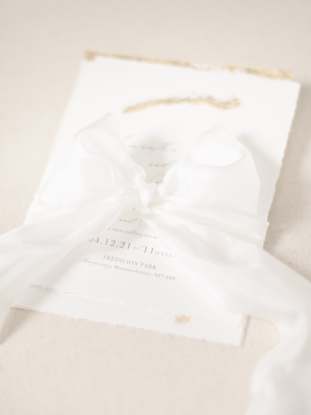Luxury paper invite written with gold ink and wrapped with silk white ribbon