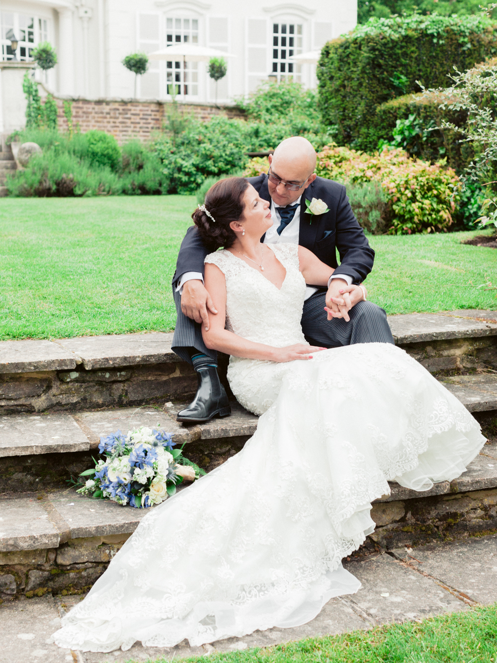 Dreamy portrait of Bride and groom sitting on the steps outside the entrance to Gorse Hill Manor