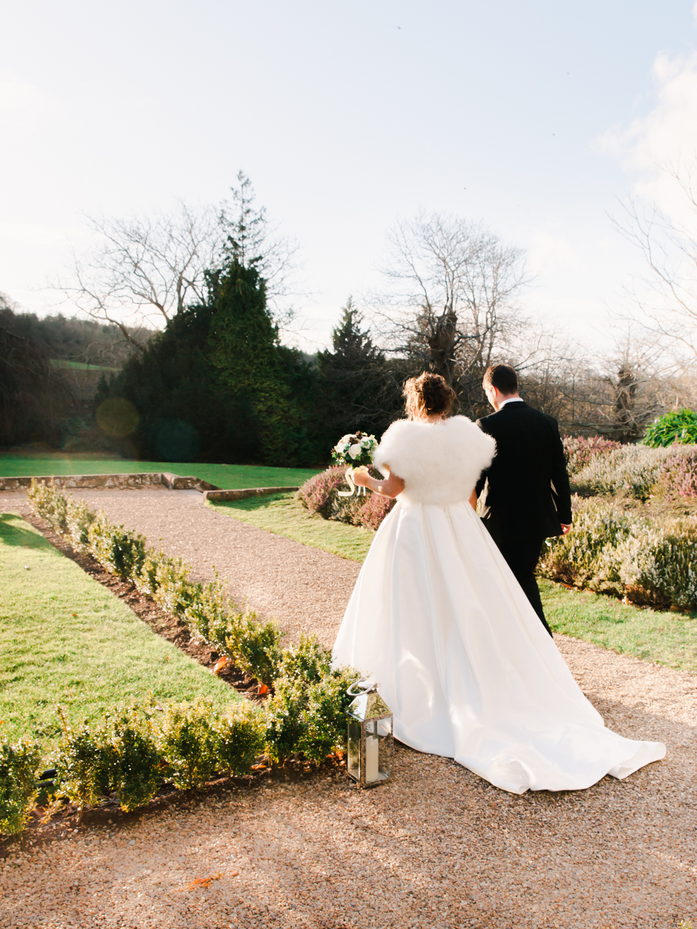 Bride and Groom walk around the country house estate on the winter day wearing white fur stole