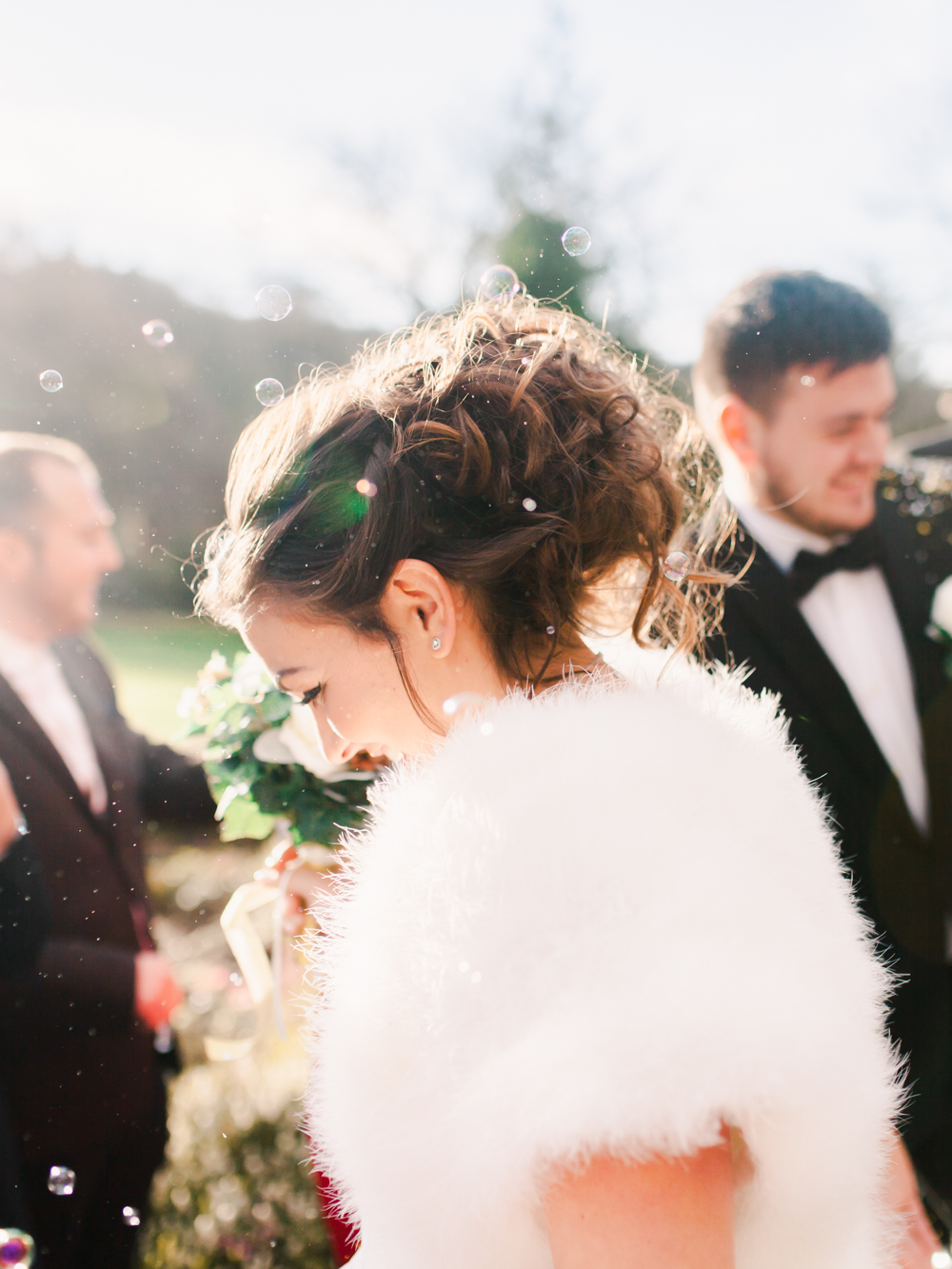 The bride walks through bubbles being blown by guests in the winter sunshine
