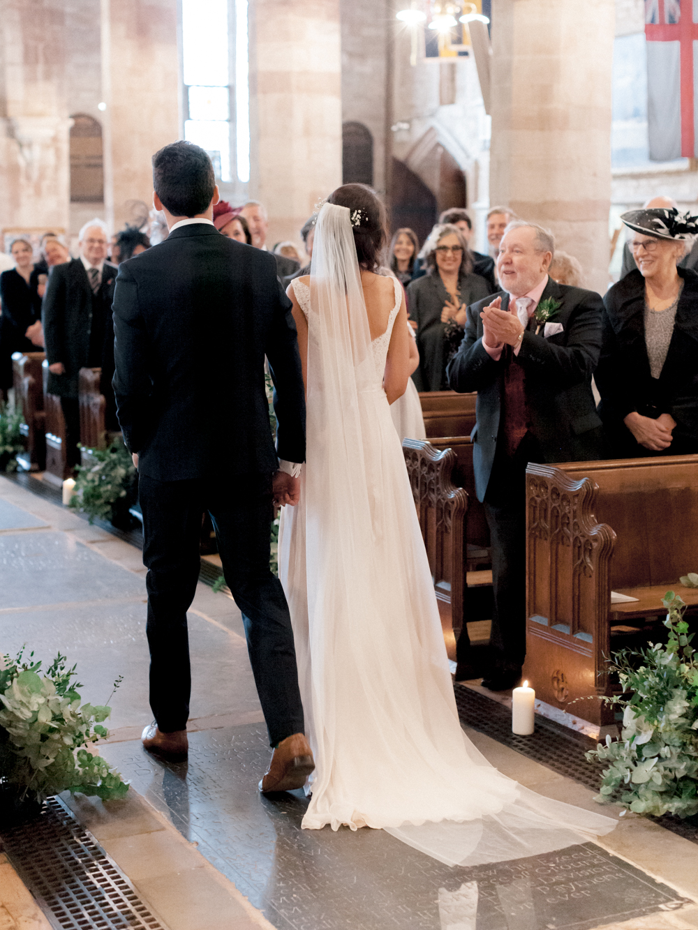 View of Bride and Groom walking up the aisle at their romantic church wedding in the Cotswolds