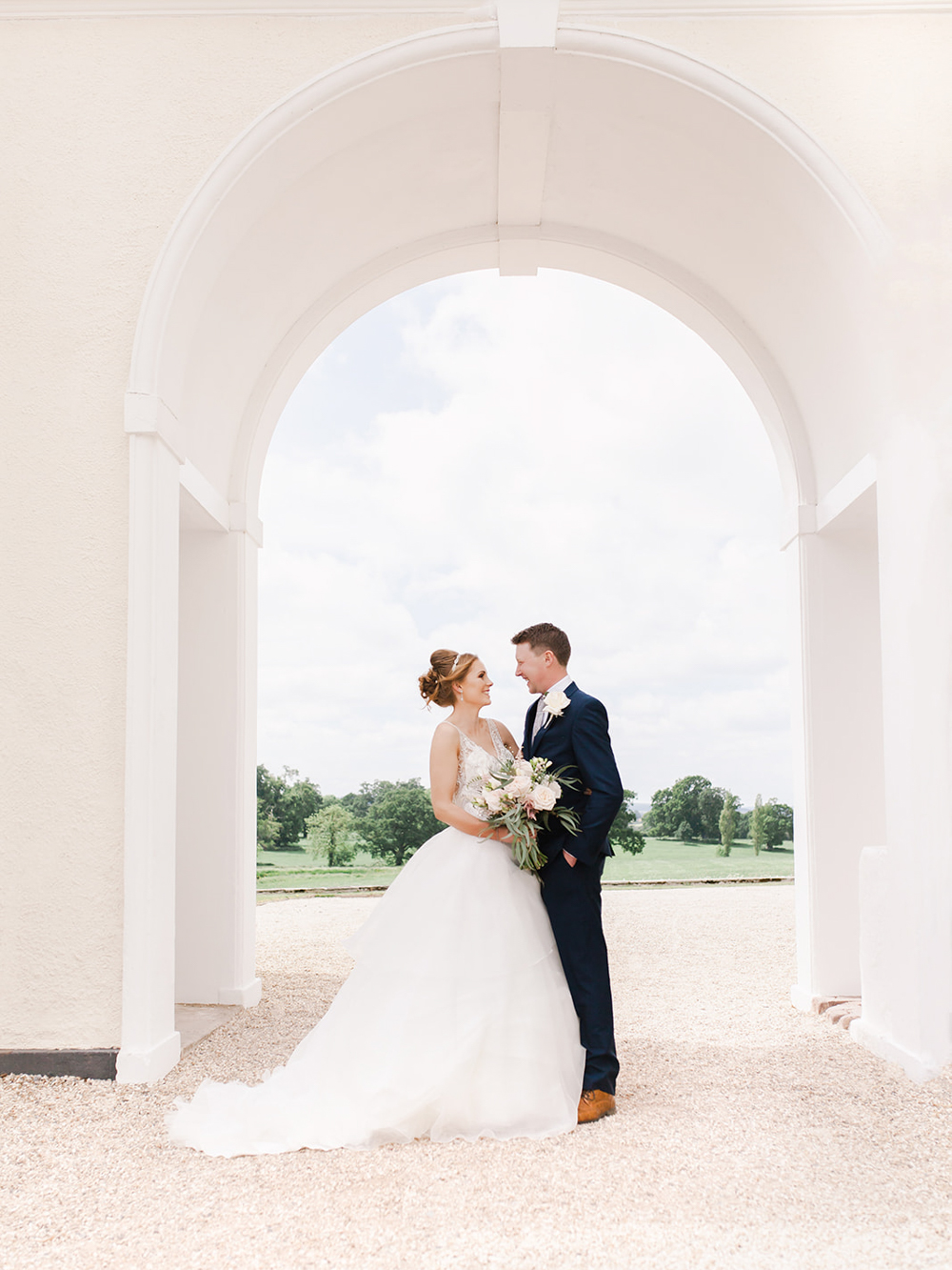 Bride and Groom stand together under the archway to Rockbeare Manor