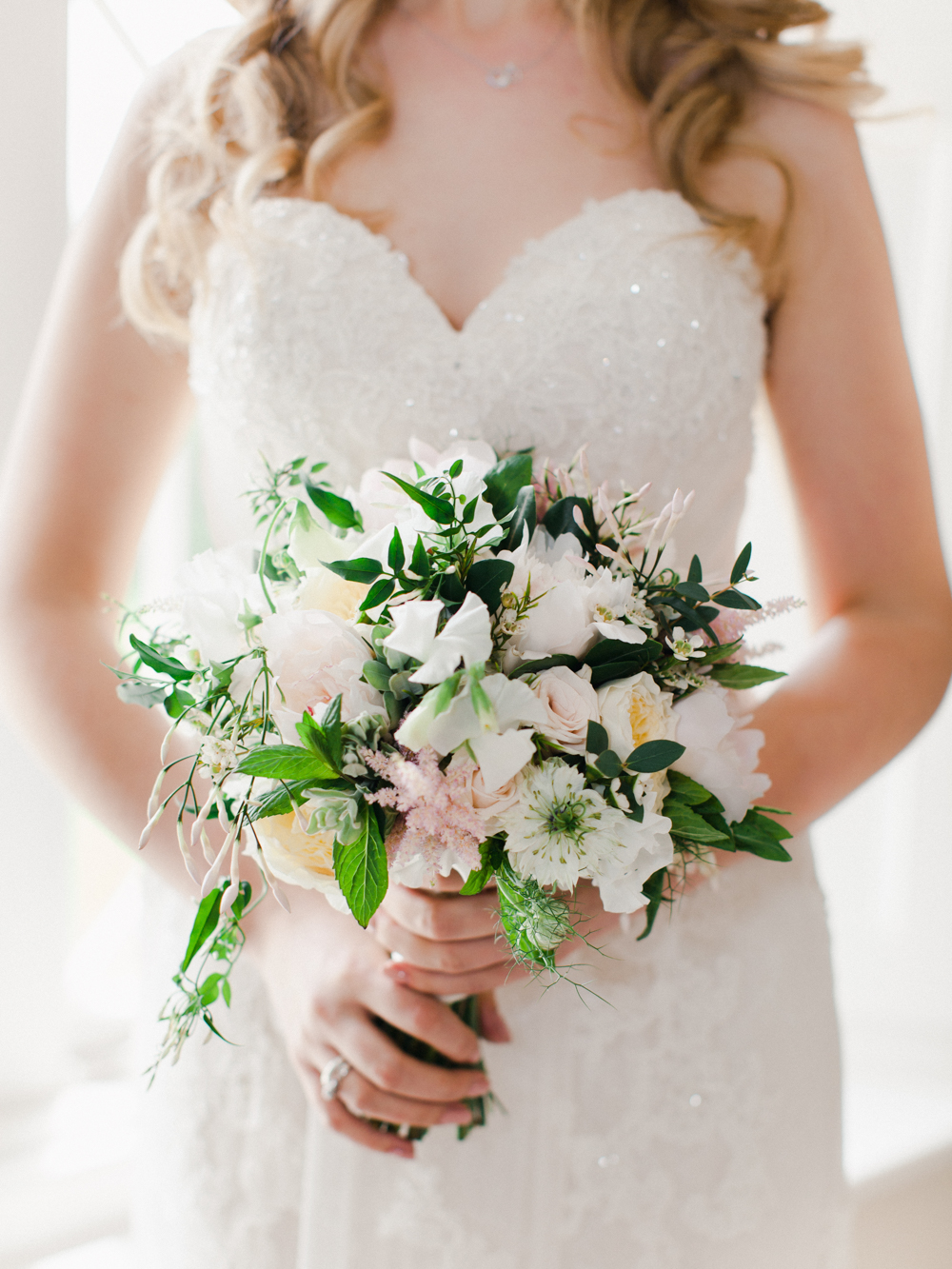 Bride holding a bouquet of blush peonies against her lace wedding dress