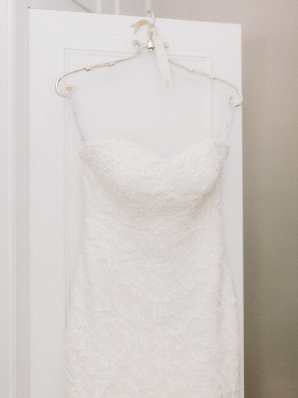 Timeless white lace wedding dress hanging from the door by an antique silver hanger