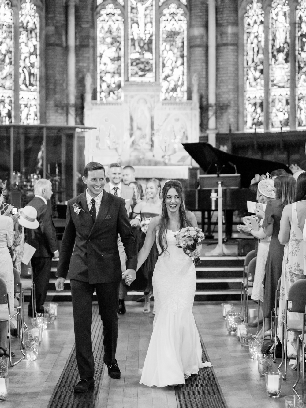 Black and White image of Bride and Groom holding hands walking down the aisle