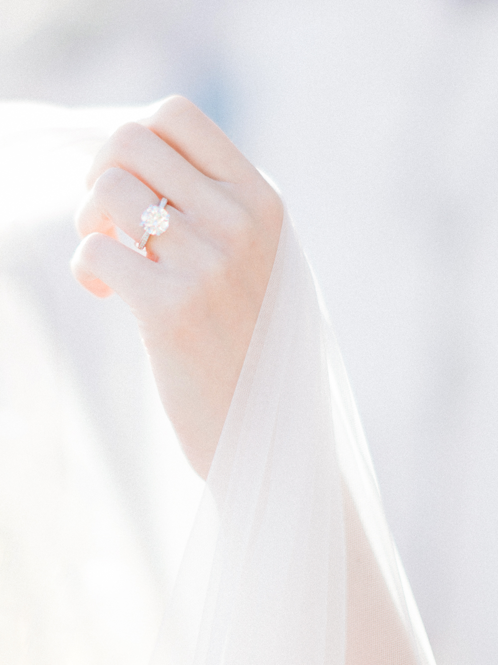 Diamond ring on the bride's finger holding a fairytale veil
