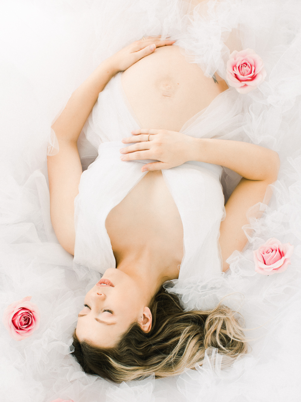 elegant woman lay in maternity dress surrounded by roses for luminous maternity portrait session in Cardiff