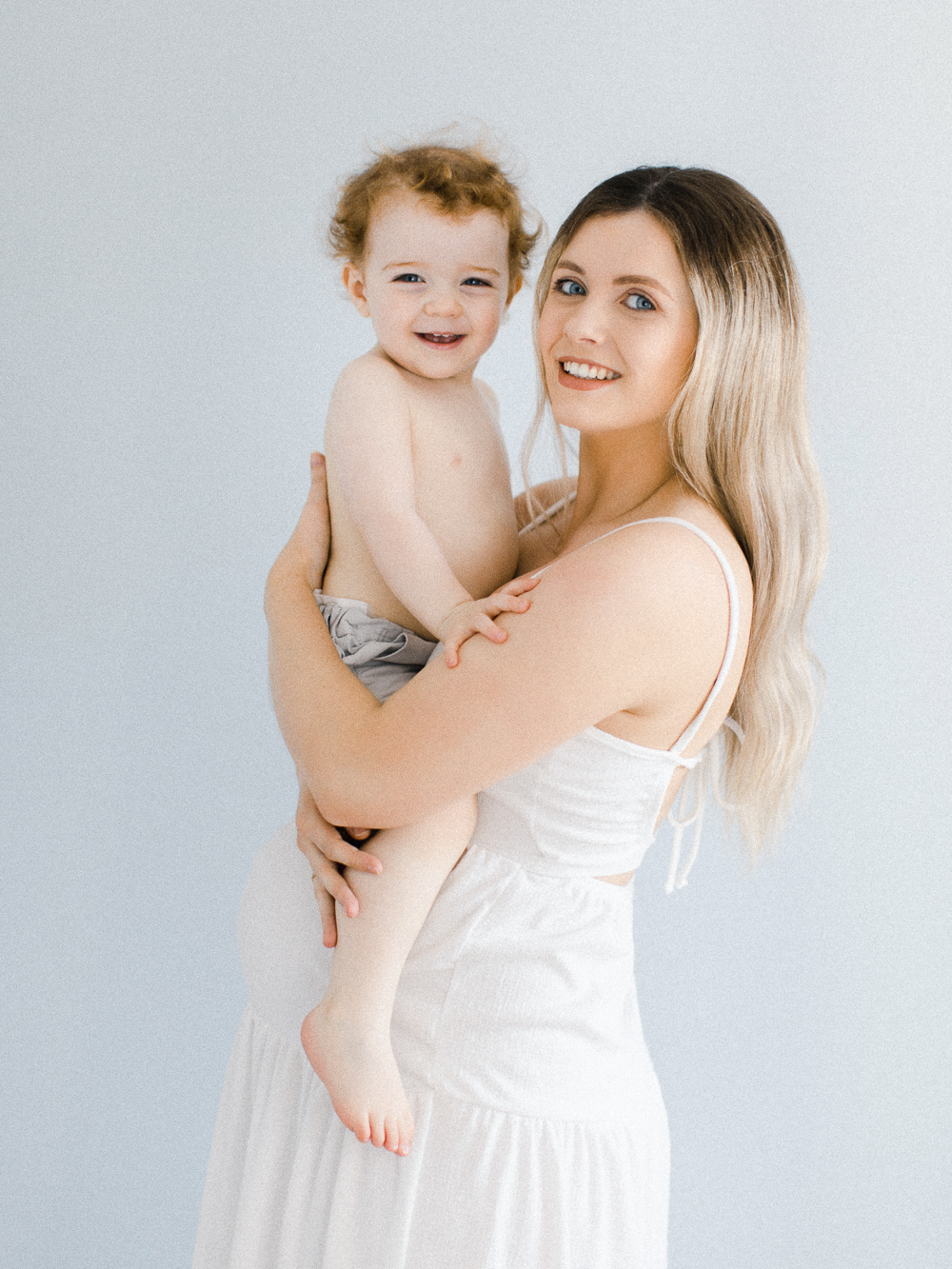 Luminous maternity portrait of pregnant mum holding her son wearing elegant white dress