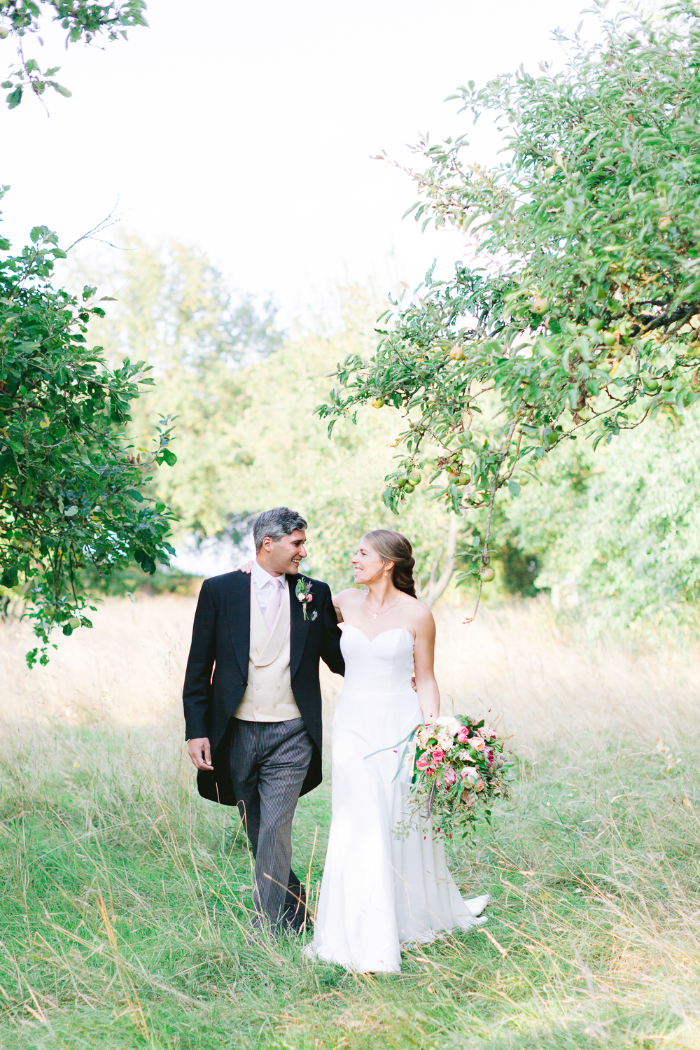 Elegant bride and groom walk through apple orchard on their wedding day
